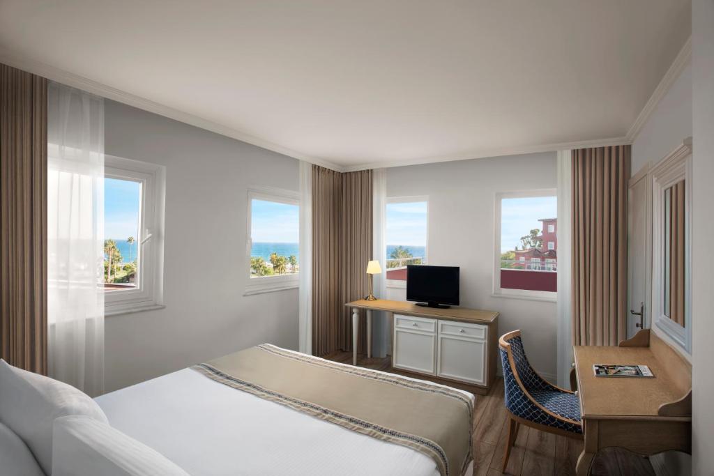 a hotel room with a bed and a desk and windows at IC Hotels Santai Family Resort - Kids Concept in Belek
