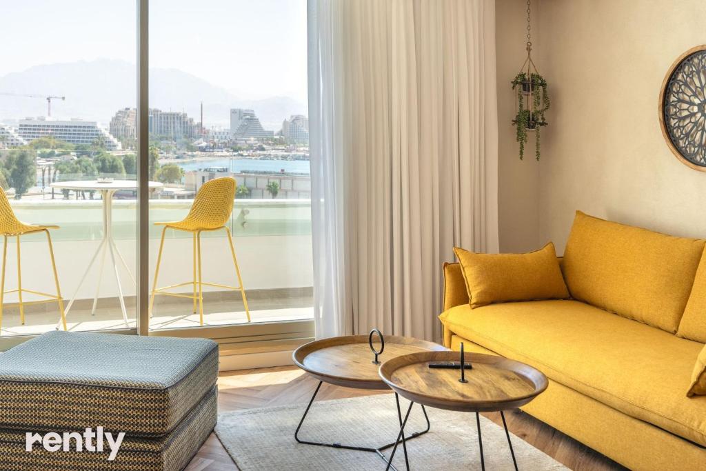 ein Wohnzimmer mit einem gelben Sofa und einem großen Fenster in der Unterkunft Luxury Apartments And Studios At Sea Side By Rently in Eilat