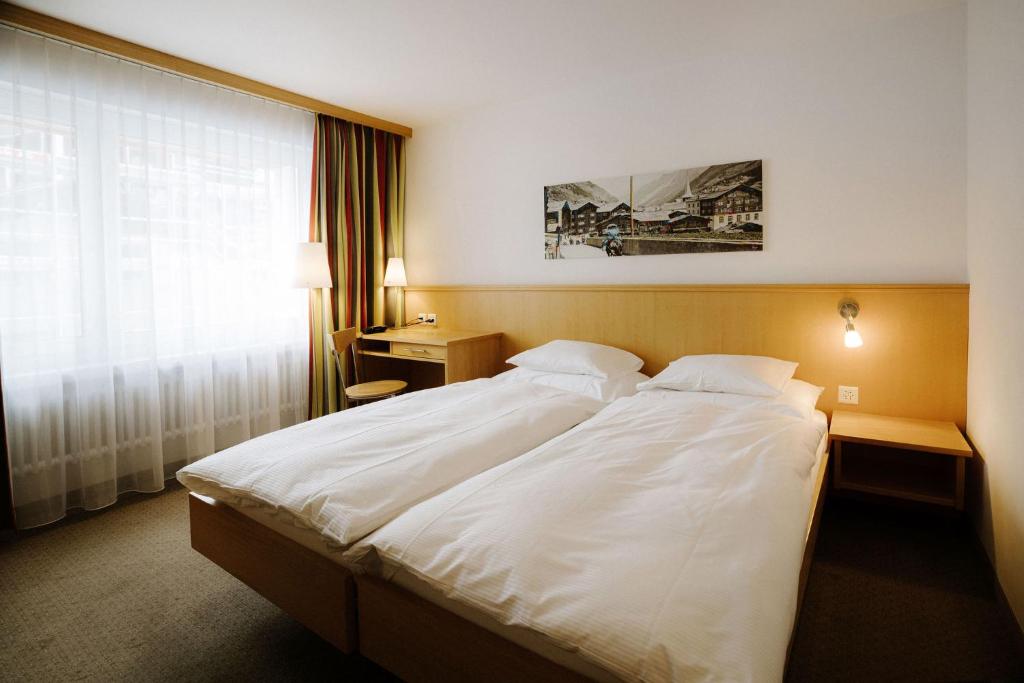 a bedroom with a large white bed with a window at Alpine Hotel Perren in Zermatt
