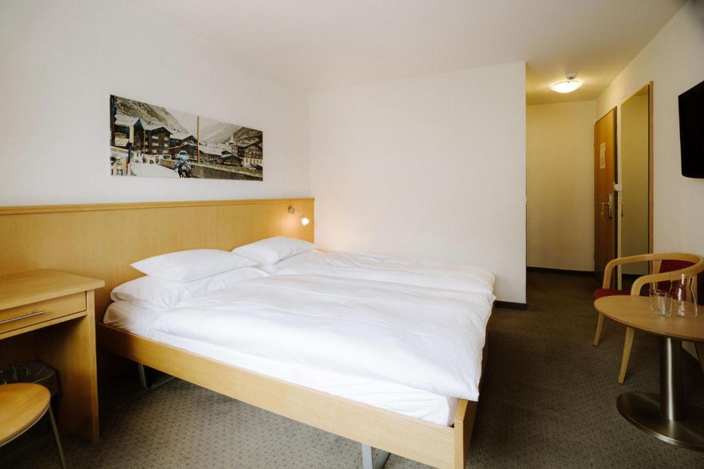 a bedroom with a white bed and a table and chairs at Alpine Hotel Perren in Zermatt
