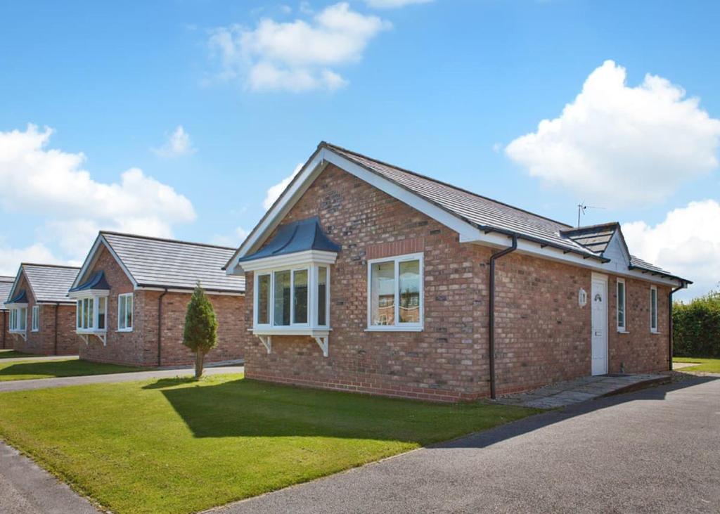 a brick house with a green lawn in front of it at Bridlington Holiday Cottages in Fraisthorpe