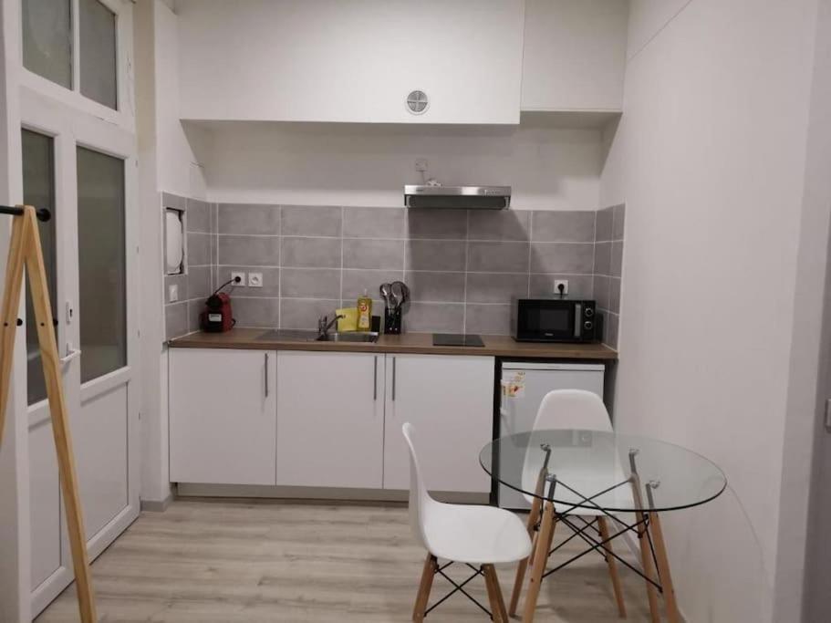 une cuisine avec une table en verre et des chaises blanches dans l'établissement Appartement T1 centre ville Carmes Metz, à Toulouse