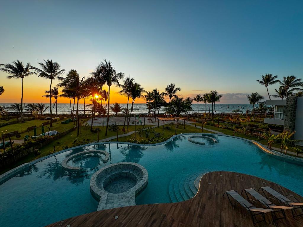 a large swimming pool with palm trees and the ocean at Naluum Milagres in Passo de Camarajibe