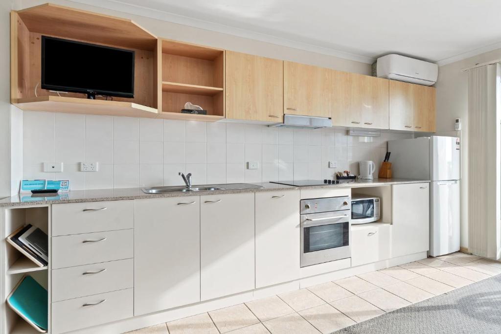 a kitchen with white cabinets and a flat screen tv at Nesuto Apartments - Unit 631 in The Entrance