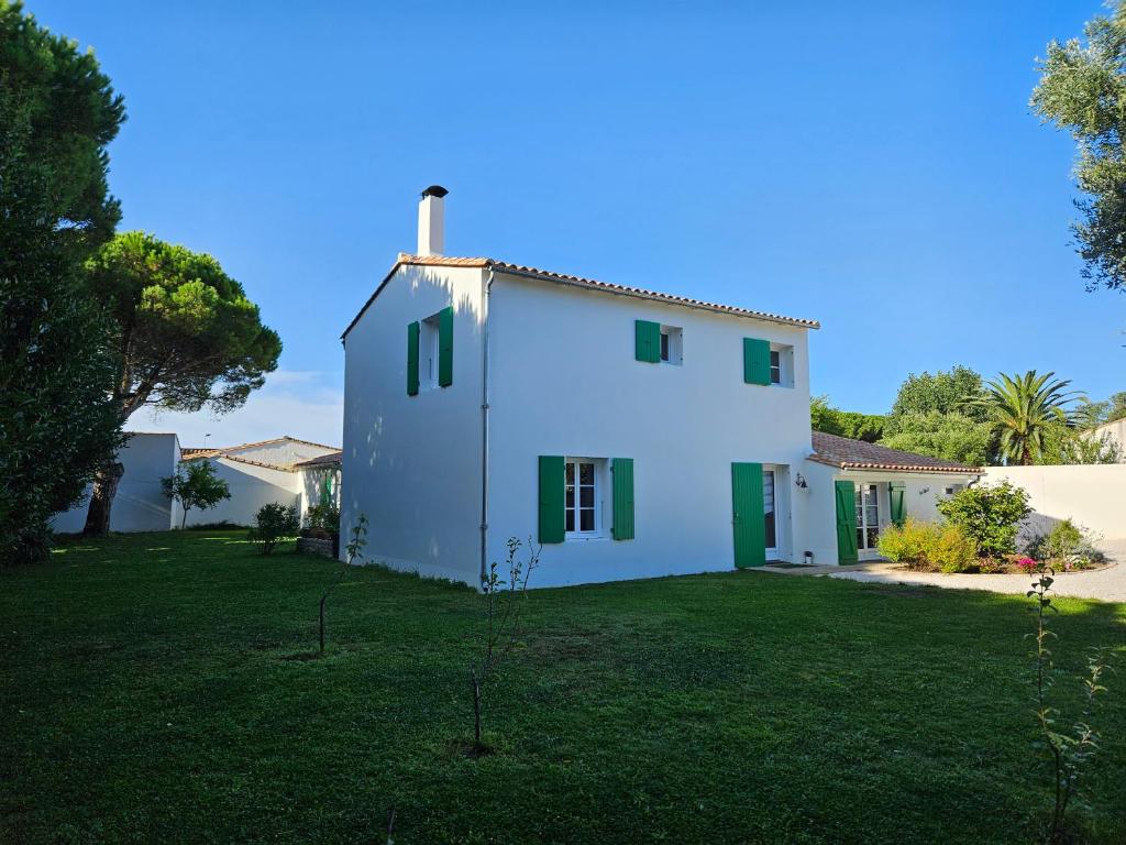 une maison blanche avec volets verts sur une cour dans l'établissement La Nout - Maison 8 personnes Bois-Plage-en-Ré, au Bois-Plage-en-Ré