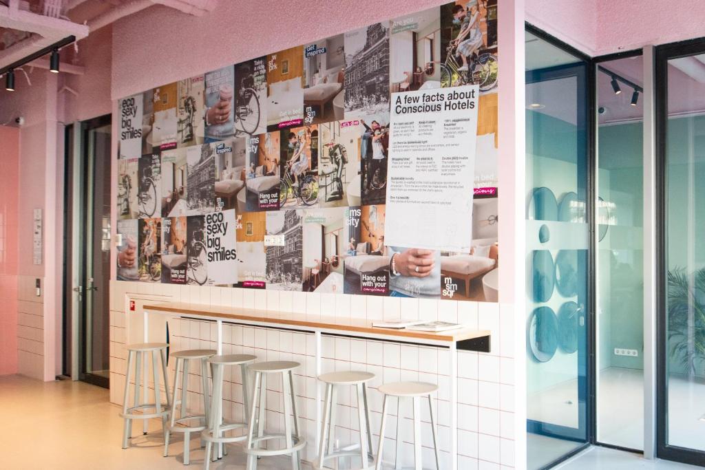 a bar with stools and a wall with posters at Conscious Hotel Vondelpark in Amsterdam