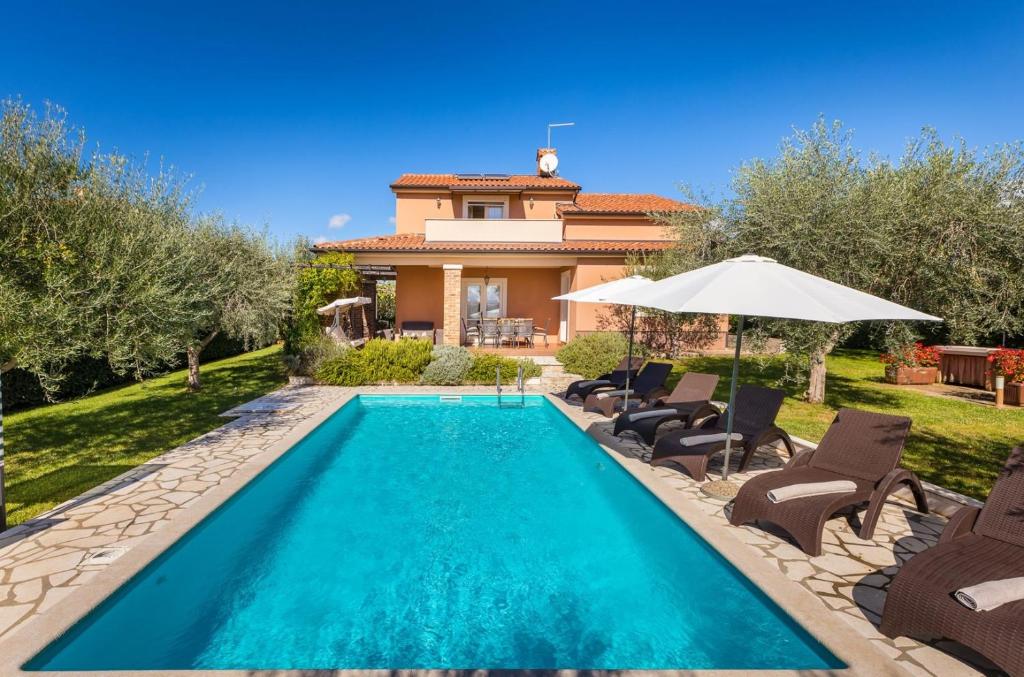 una piscina di fronte a una casa con sedie e ombrellone di Villa Klara a Kaštelir (Castellier)