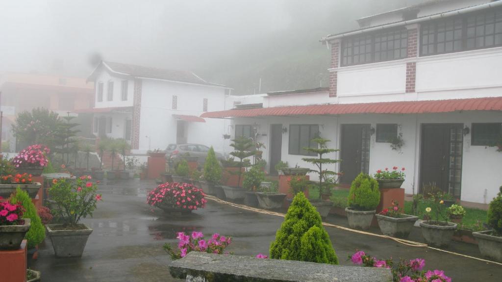 un cortile bagnato dalla pioggia con case e fiori sotto la pioggia di Trilan Cottages - Donnington Road a Kotagiri