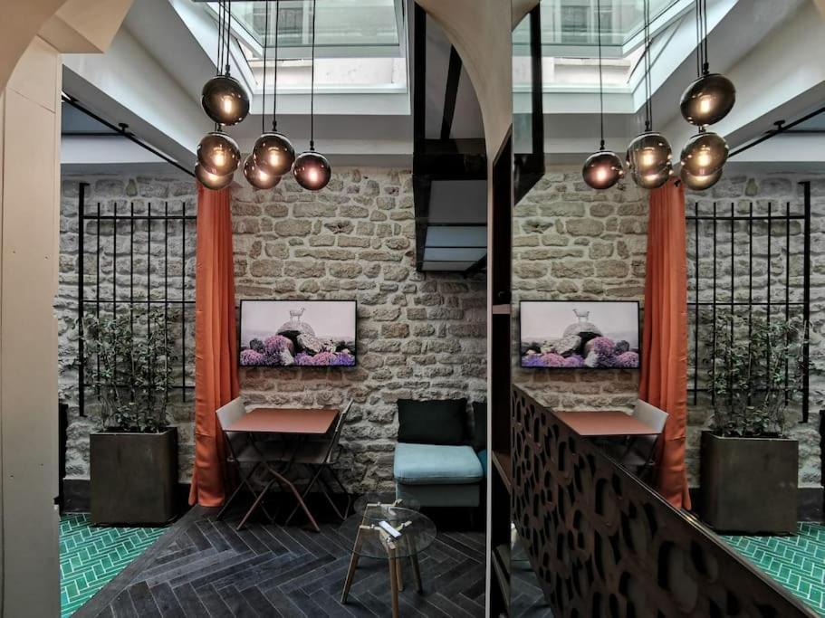 un hall avec deux tables et un mur en briques dans l'établissement Le Petit Atelier Des Lumières, VÉRANDA AGRÉABLE, à Paris