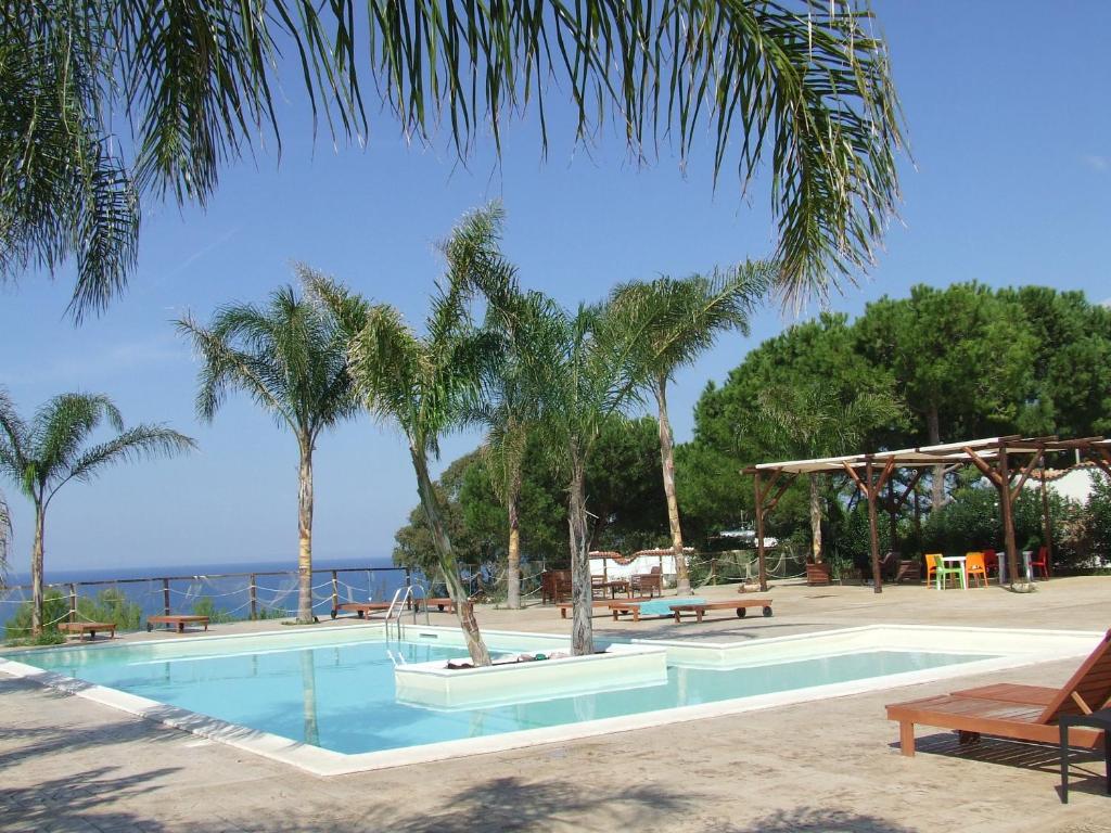 a swimming pool with palm trees next to the ocean at Petruso Resort in Balestrate
