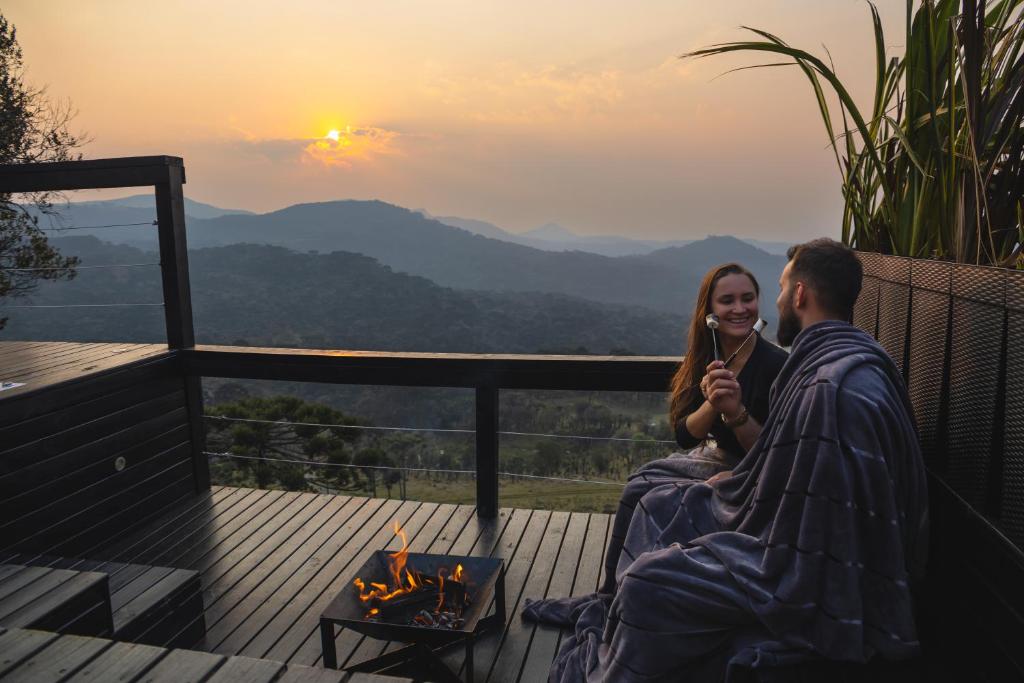 a man and a woman sitting on a deck looking at the sunset at Cabanas Duas Faces - Urubici in Urubici