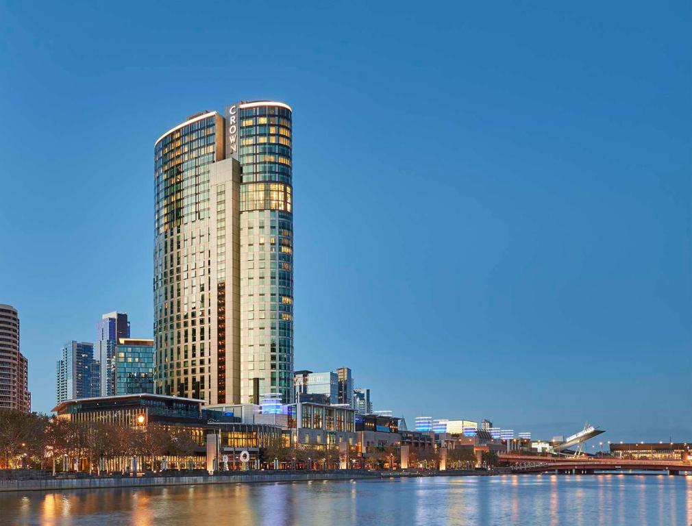 a tall building next to a river with a city at Crown Towers Melbourne in Melbourne