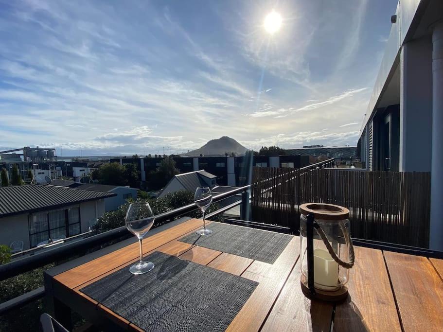 un tavolo in legno con 2 bicchieri da vino sul balcone di Sunset Apartment, Mount views, POOL, GYM, HOT TUB a Mount Maunganui