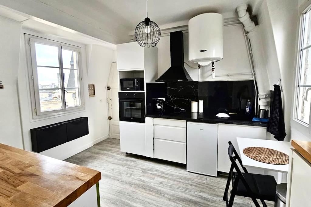 une cuisine avec des armoires blanches et une table à l'intérieur dans l'établissement Appartement vue tour Eiffel ligne 14 à côté de Paris, à Gentilly