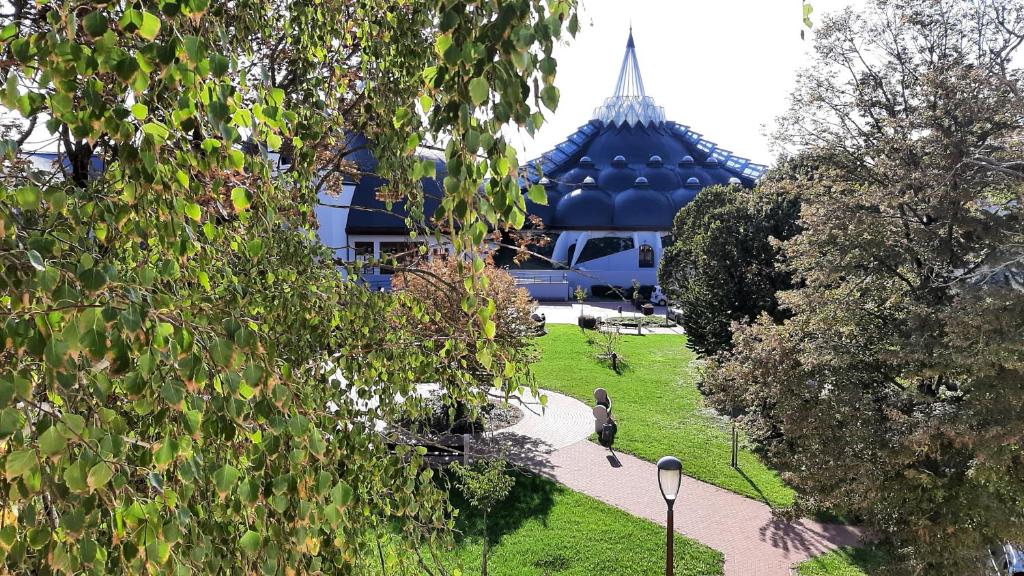 a building with a blue roof and a path in a park at Arcanum Apartman in Makó