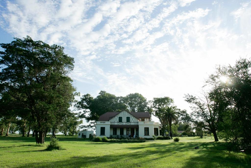 une maison blanche sur un champ verdoyant avec des arbres dans l'établissement Hotel Rural La Pampeana, à Sarah