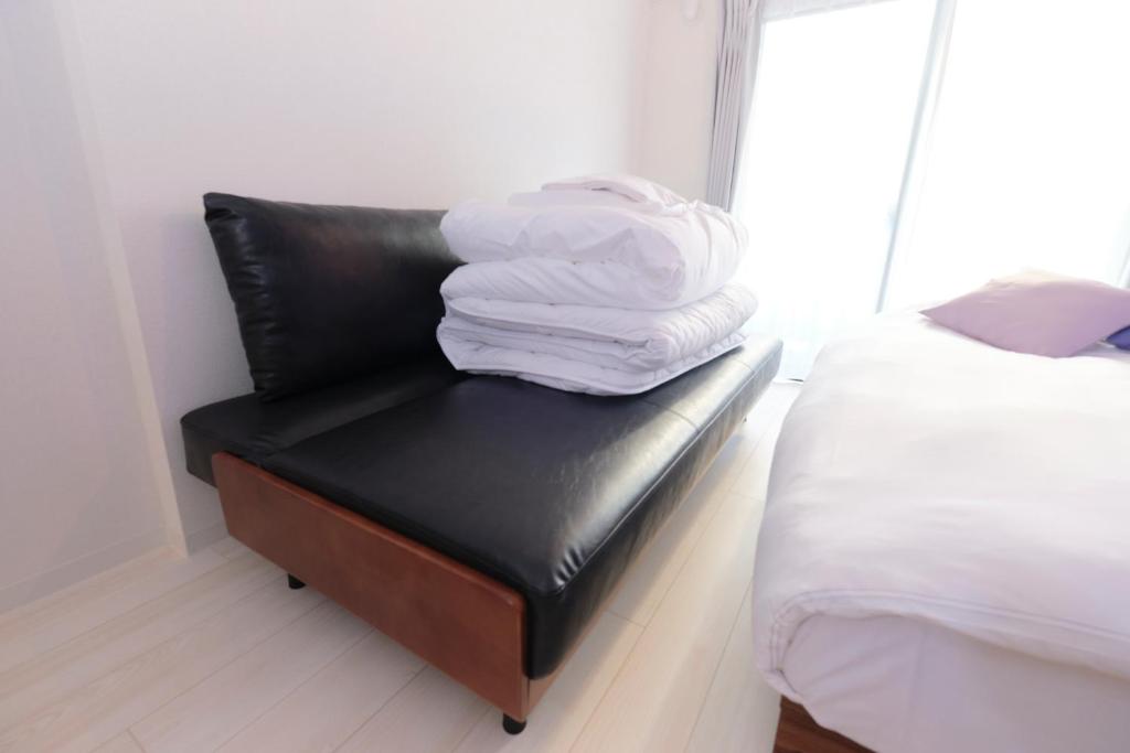 a pile of towels sitting on a leather chair next to a bed at RIZOTIA Hakusan by Tranova in Tokyo
