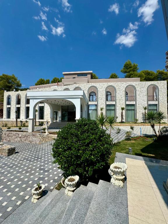 Un gran edificio blanco con un árbol delante. en Hotel Panorama &amp; Spa Elbasan, en Elbasan