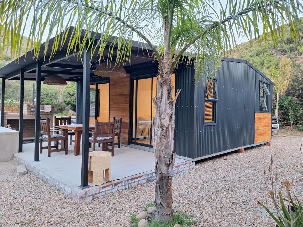 una piccola casa nera con un tavolo e un albero di Believe Cottage a Oudtshoorn