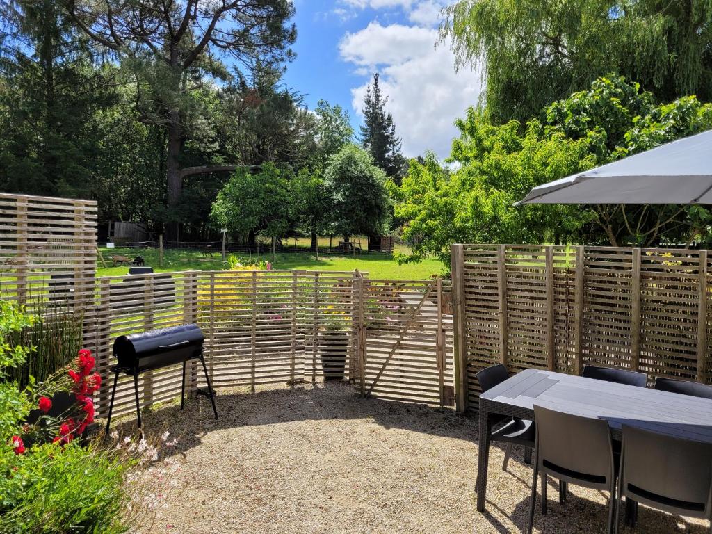 Un jardín con valla de madera, mesas y sombrilla. en Gîte Ty Laouen Clohars-Carnoët, en Clohars-Carnoët