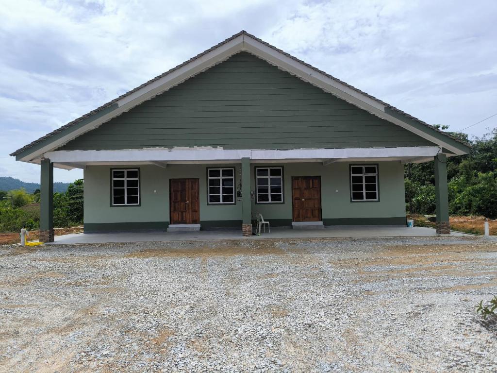a green house with brown doors and a gravel driveway at Natures Haven Homestay II in Kampong Lubok Panjang