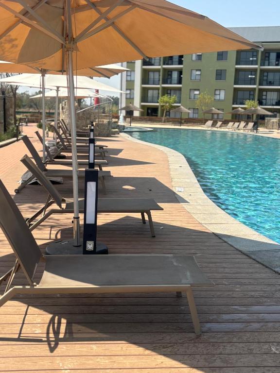 a row of chairs and umbrellas next to a pool at Cozy nest apartment in Pretoria
