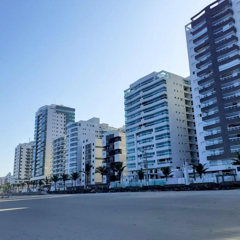 a row of tall buildings with palm trees in front at AP Padrão Pé na Areia Centro TOP TODO COM AR CONDICIONADO in Mongaguá
