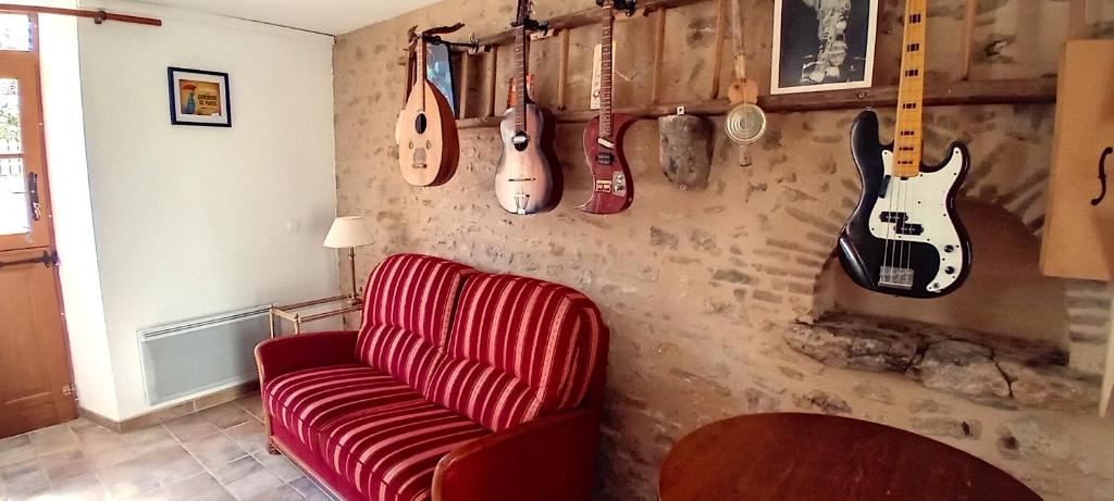 a living room with a red couch and guitars on the wall at Charmante petite maison pour deux in Badecon-le-Pin