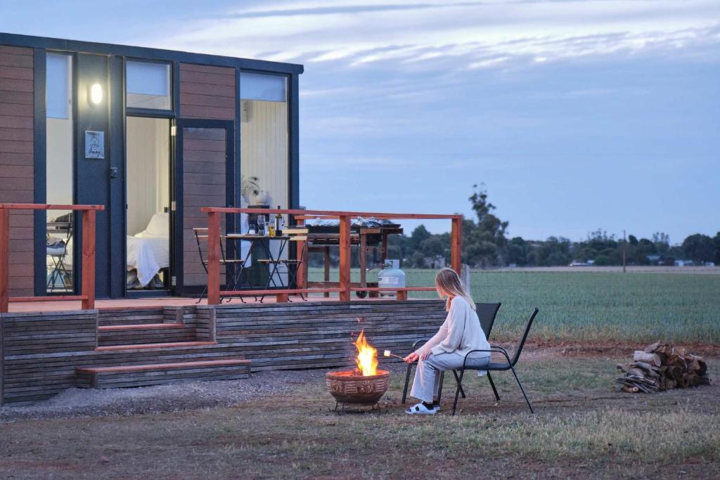 a woman sitting on a chair by a fire in front of a house at The Gums Cottage by Tiny Away in Hallett