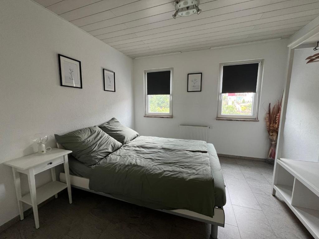 a bedroom with a bed and a table and two windows at FeWo NguyenCao in Markdorf