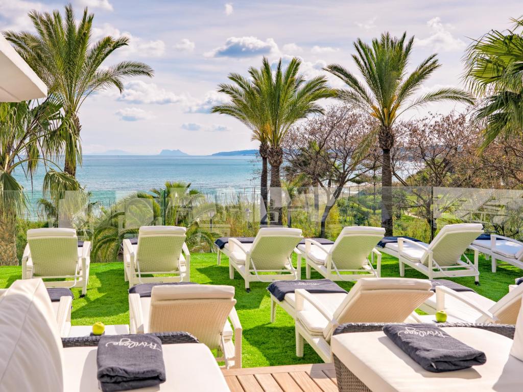 a patio with white chairs and palm trees at H10 Estepona Palace in Estepona