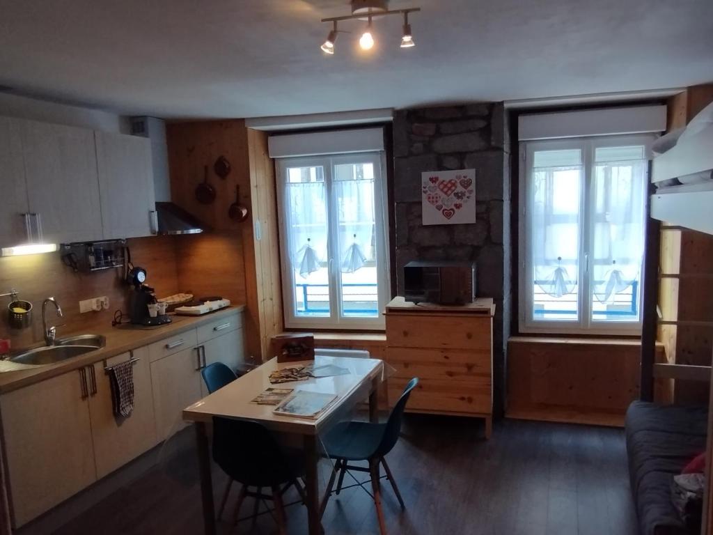 une cuisine avec une table, des chaises et des fenêtres dans l'établissement Studio au cœur du centre ville, à Le Mont-Dore