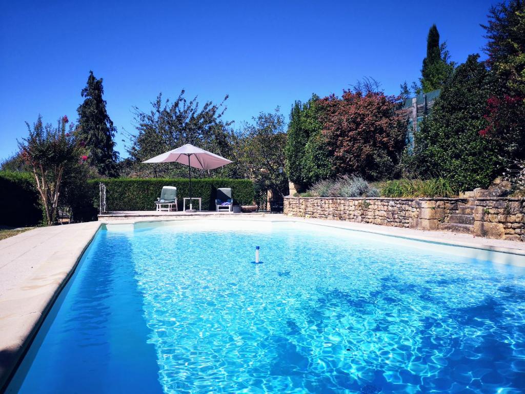 - une piscine bleue avec une table et un parasol dans l'établissement Maison typique avec piscine privée - 6km Sarlat, à Saint-André-dʼAllas