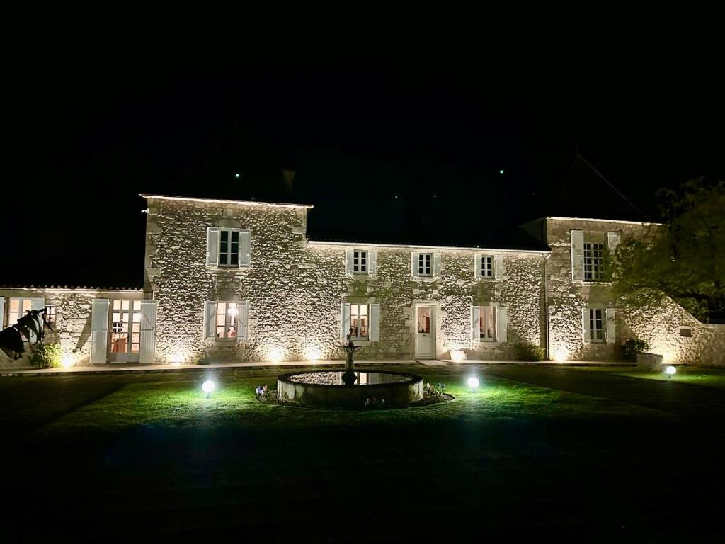- un grand bâtiment en pierre avec une fontaine devant lui la nuit dans l'établissement Château de Lafont Suites, à Saint-Vivien