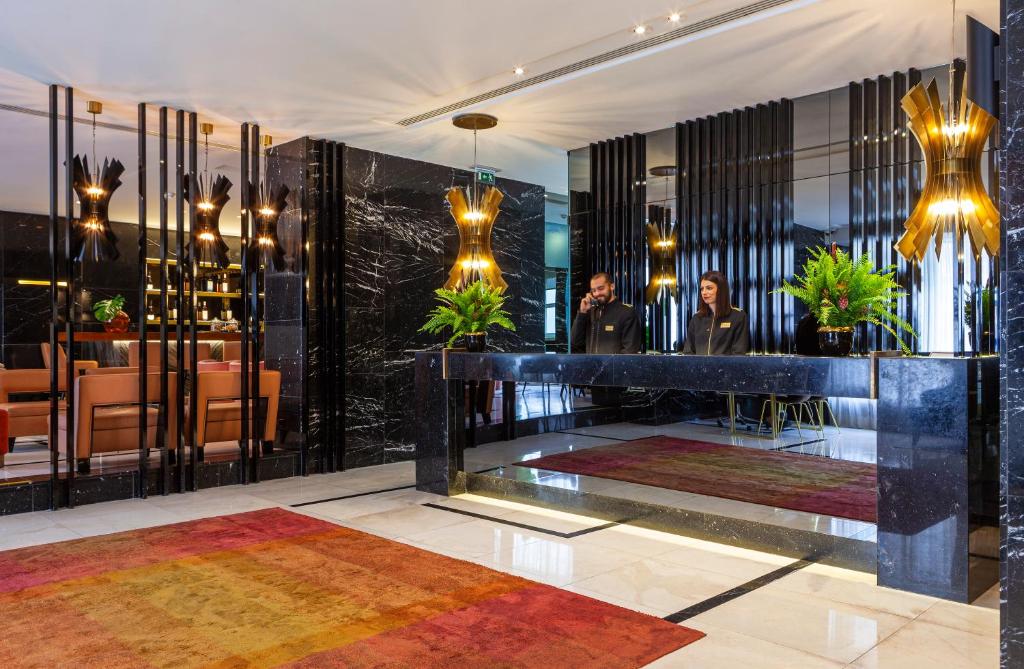 A polished reception lobby combines a black marble desk, reflective walls, dramatic lamps, and a bar or dining area.