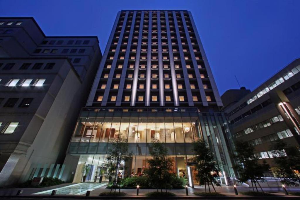 a tall building with many windows in a city at HOTEL UNIZO Osaka Yodoyabashi in Osaka