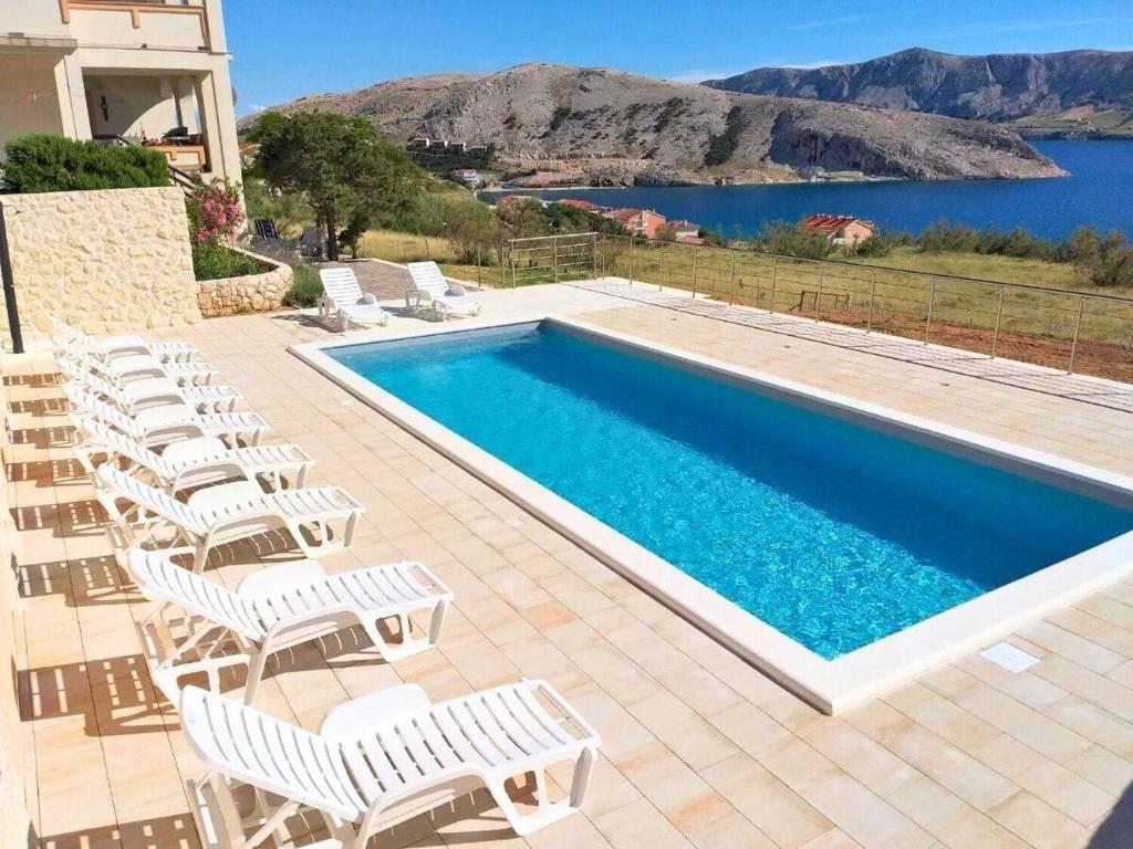 a swimming pool with white chairs next to a house at Apartments PoolHouse in Metajna
