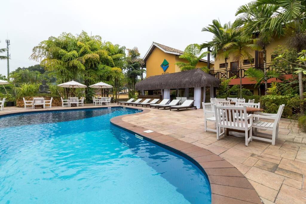 a swimming pool with chairs and tables and a building at Flat em llhabela no Ilha Flat Hotel in Ilhabela