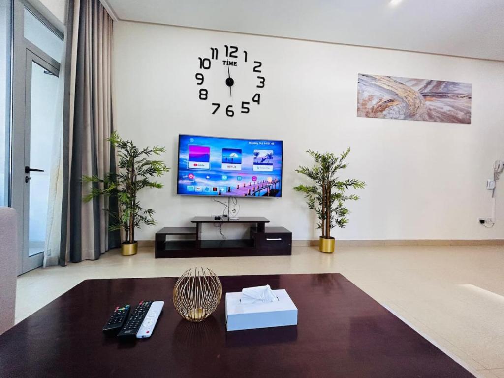 a living room with a tv and a clock on the wall at Aspire Tower - Breezy Two Bedroom in Juffair in Manama