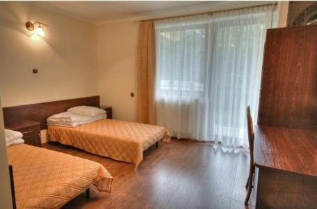 Room with twin beds, large window with sheer curtains, and wooden flooring.