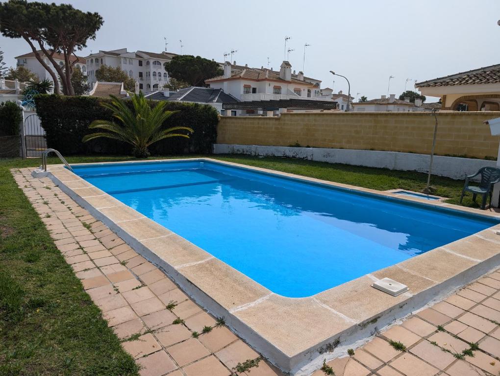 a swimming pool with blue water in a yard at Chalet adosado en Matalascañas con piscina y chimenea, cerca de la playa in Matalascañas