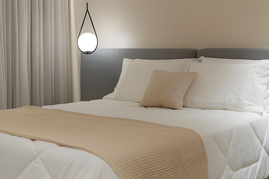 ein weißes Bett mit weißen Kissen und einer Lampe in der Unterkunft Lofts amplos e sofisticados a 600m da Vila Germânica in Blumenau