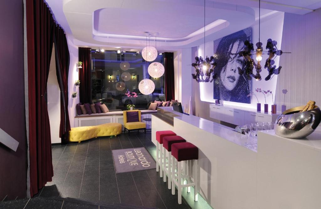 a room with a bar with red chairs and a living room at Leonardo Boutique Hotel Munich in Munich