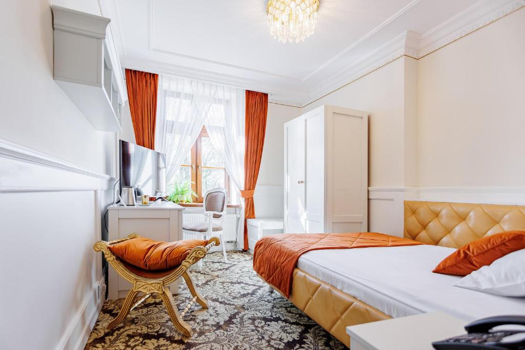 Cozy room with orange bedspread and curtains, white wardrobe, ornate gold-footed bench.