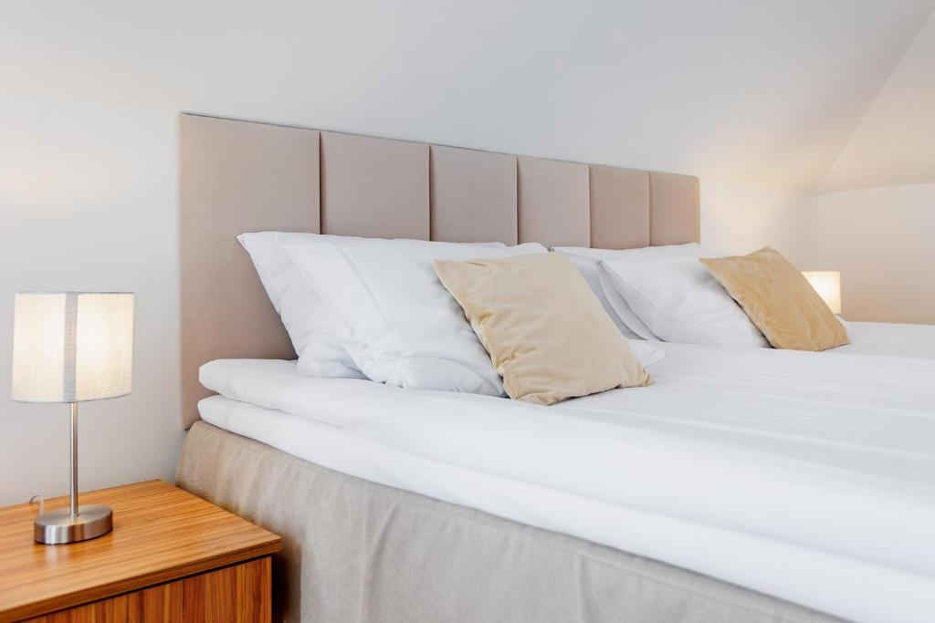 Close-up of neatly made bed with padded beige headboard, soft pillows, wooden nightstand lamp.