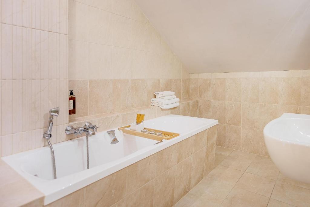 Built-in bathtub in beige tiled bathroom with wooden bath tray, stacked white towels, sloped ceiling.