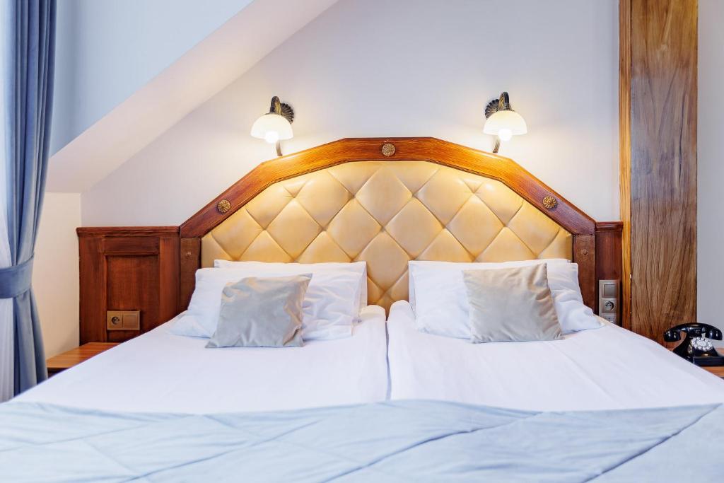 Twin beds pushed together under tufted leather headboard, warm bedside lamps, pale drapes, vintage telephone.
