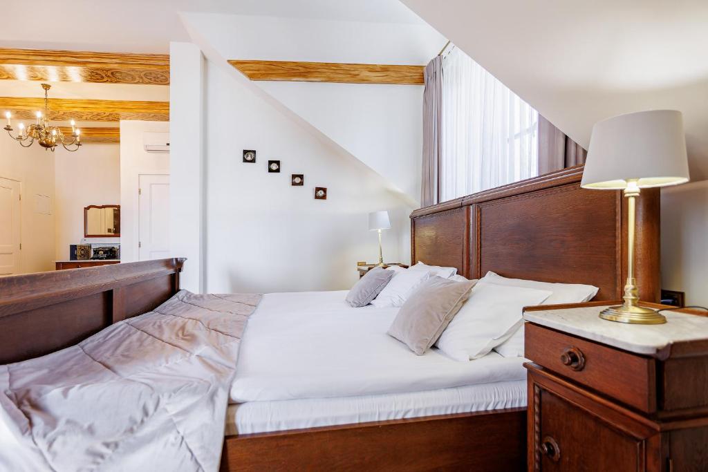 Wooden-framed bed in bright room with bedside lamp, carved furniture, soft layered bedding.