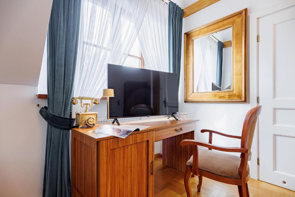 Wooden desk topped with flat-screen TV, decorative gold telephone, framed mirror and wooden chair.