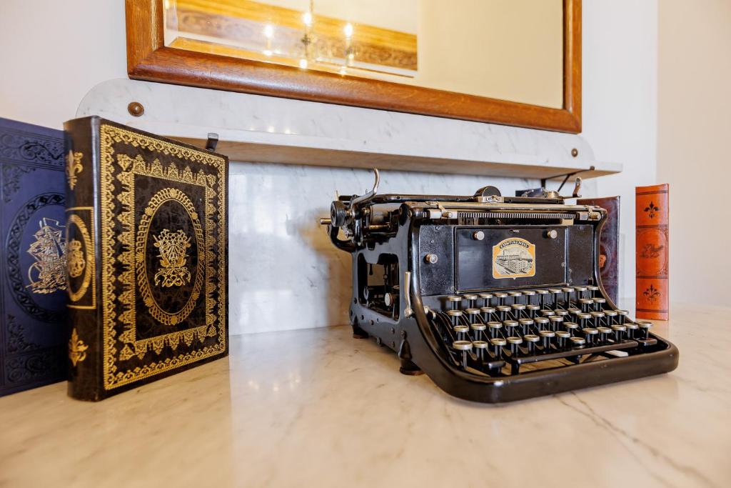 Vintage black typewriter displayed on marble dresser beside ornate leather-bound books and mirror.